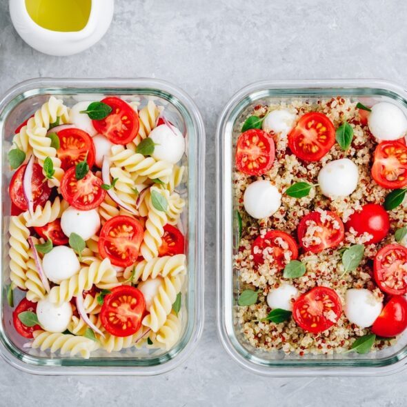 Meal prep containers with pasta salad or quinoa, tomatoes, mozzarella cheese, and basil.