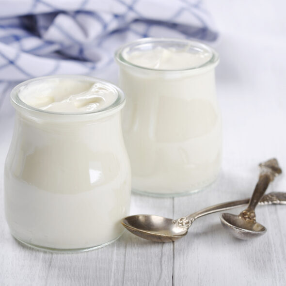 Greek yogurt in a glass jars with spoons on wooden background